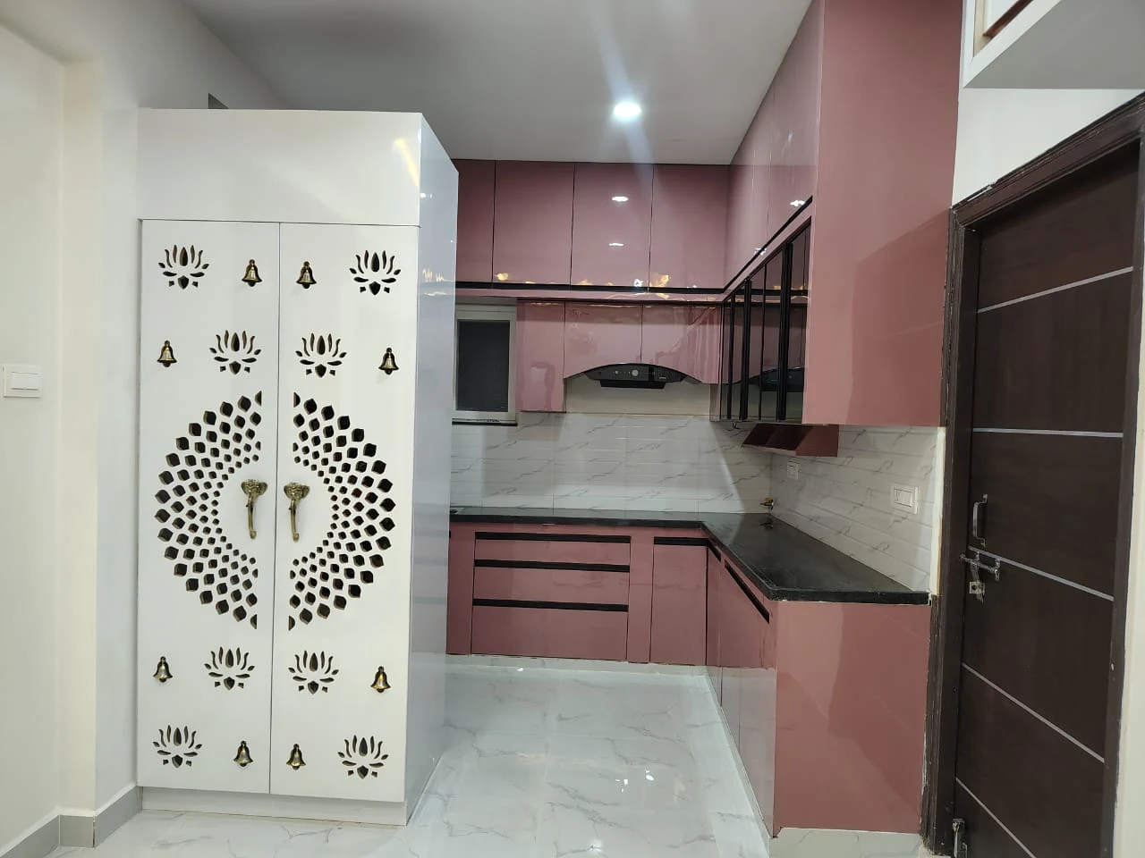 Modern blush pink rose acrylic modular kitchen with black countertop and jali mandir by Avika Interior Patna